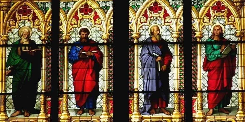 Stained glass window depicting four figures holding books and scrolls, dressed in red, blue, green, and purple robes, framed by ornate gothic arches.